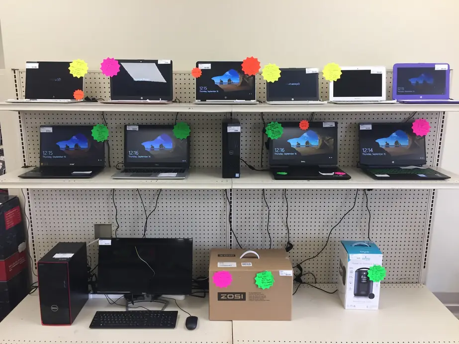 Shelf of pre-owned laptops and desktop computers with handwritten price stickers at Express Pawn Paragould